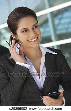 Stock Image - Businesswoman using mobile phone outdoors. Fotosearch