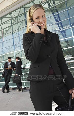 Stock Photo - Businesswoman using mobile phone with coworkers in background. Fotosearch