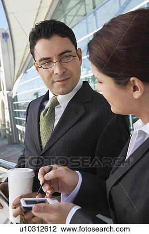 Businesswoman using PDA next to businessman with take away coffee, outdoors View Large Photo Image Stock Image - Businesswoman using PDA next to businessman with take away coffee, outdoors. Fotosearch