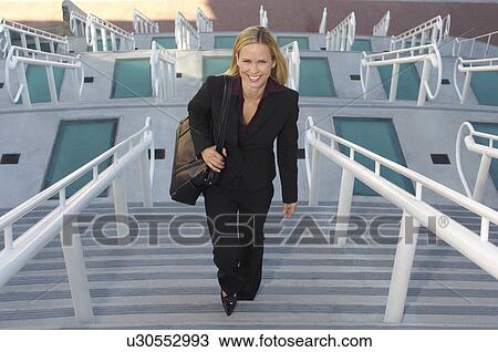 Stock Image - Businesswoman walking up stairs, elevated view. Fotosearch