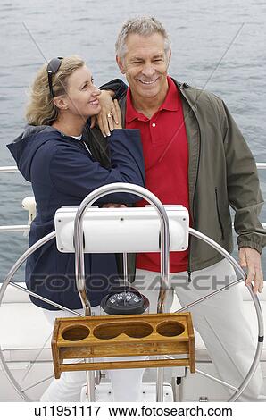 Stock Photo - Couple at helm of sailboat, smiling. Fotosearch
