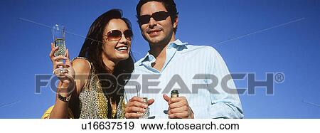 Stock Photo - Couple celebrating with champagne outdoors, portrait. Fotosearch