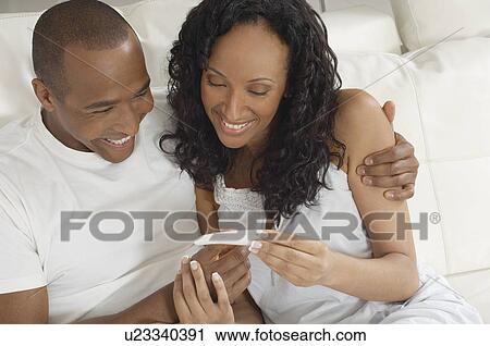 Stock Image - Couple examining pregnancy test in bed. Fotosearch