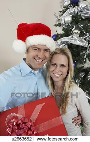 Couple holding present in front of Christmas tree View Large Photo Image Stock Image - Couple holding present in front of Christmas tree. Fotosearch