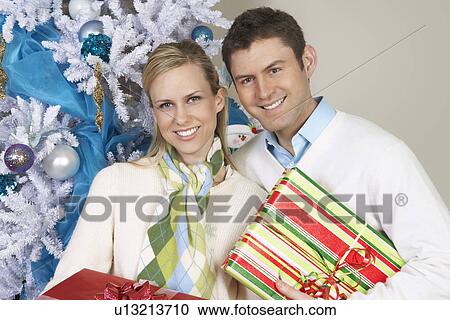 Couple holding presents by Christmas tree, portrait View Large Photo Image Stock Image - Couple holding presents by Christmas tree, portrait. Fotosearch