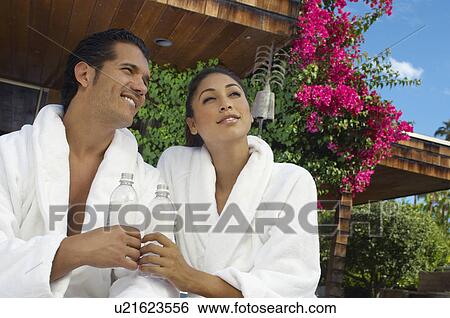 Stock Photograph - Couple in bathrobes holding water bottles and looking away on porch. Fotosearch