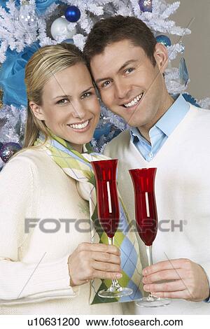 Couple toasting champagne glasses by Christmas tree, portrait View Large Photo Image Stock Image - Couple toasting champagne glasses by Christmas tree, portrait. Fotosearch