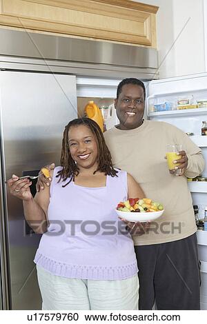 Stock Image - Couple with food and drink by open fridge. Fotosearch
