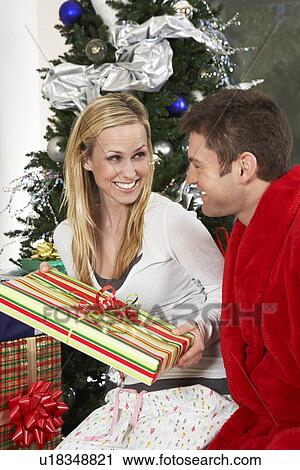 Couple with present by Christmas tree View Large Photo Image Stock Image - Couple with present by Christmas tree. Fotosearch