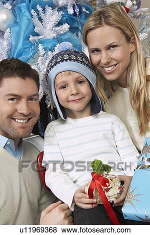 Couple with son (5-6) holding present in front of Christmas tree View Large Photo Image Stock Photo - Couple with son (5-6) holding present in front of Christmas tree. Fotosearch
