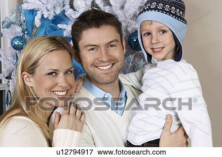 Stock Photo - Couple with son (5-6) in front of Christmas tree, portrait. Fotosearch