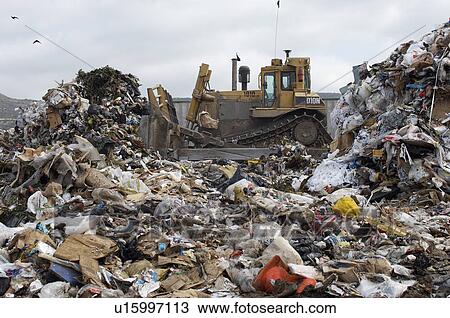 Stock Image - Digger moving waste at landfill site. Fotosearch