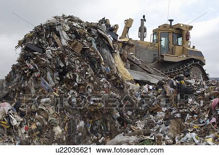 Stock Image - Digger moving waste at landfill site. Fotosearch