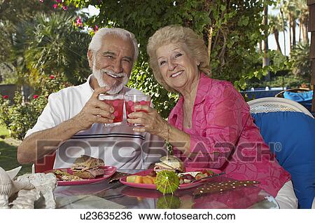 Stock Photograph - Elderly couple with drinks in garden. Fotosearch