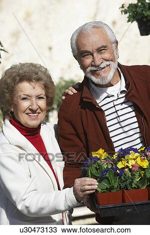 Stock Image - Elderly man and senior woman holding tray with potted flowers. Fotosearch