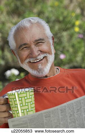 Stock Image - Elderly man reading newspaper outdoors, portrait. Fotosearch