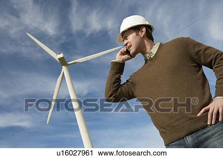 Stock Image - Engineer using mobile phone at wind farm. Fotosearch