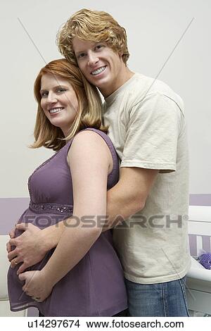 Picture - Expectant couple embracing at home, portrait. Fotosearch