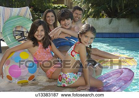 Stock Photo - Family with two girls and boy with inflatable rafts sitting by swimming pool, portrait. Fotosearch
