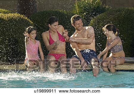 Stock Image - Family with two girls splashing, at edge of swimming pool. Fotosearch