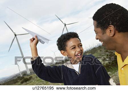 Stock Photography - Father and son (7-9) playing with paper plane at wind farm. Fotosearch