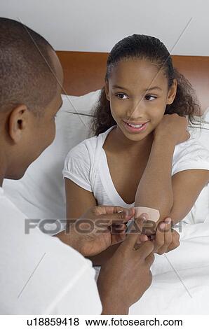 Stock Photo - Father applying bandaid to daughter (7-9) in bed. Fotosearch