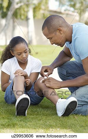 Stock Photograph - Father applying bandaid to daughter (7-9) in park. Fotosearch
