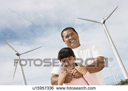 Stock Photograph - Father embracing daughter (7-9) at wind farm, portrait. Fotosearch
