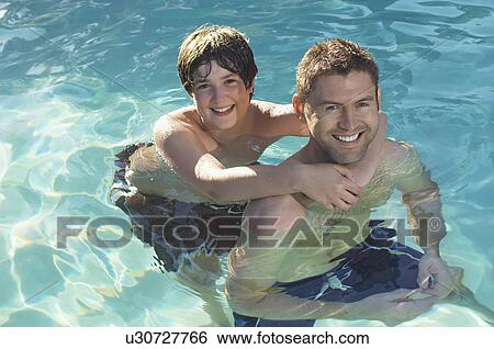 Stock Photograph - Father giving son piggy back in swimming pool, portrait. Fotosearch