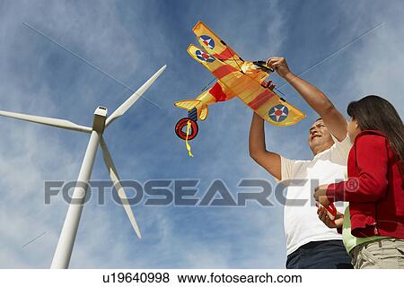 Stock Photo - Father holding airplane kite with daughter (7-9) at wind farm. Fotosearch
