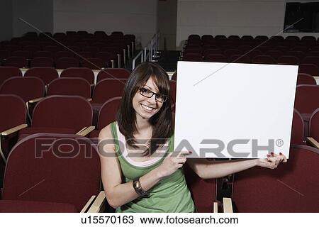Stock Image - Female student holding blank board in lecture theatre, portrait. Fotosearch