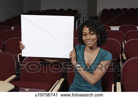 Stock Image - Female student holding blank board in lecture theatre, portrait. Fotosearch