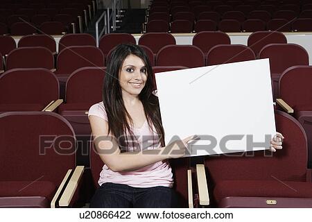 Stock Image - Female student holding blank board in lecture theatre, portrait. Fotosearch
