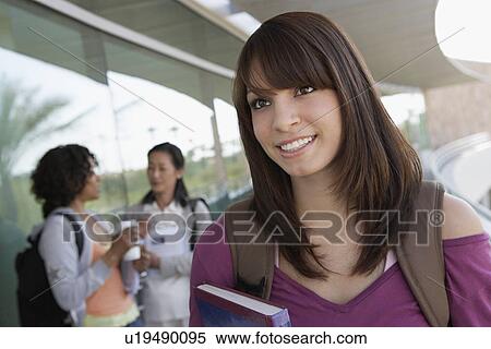 Stock Photography - Female student holding book at school, smiling. Fotosearch