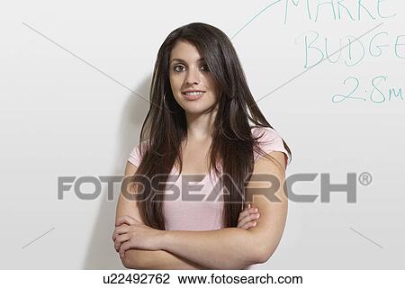 Stock Image - Female student standing by white board, portrait. Fotosearch