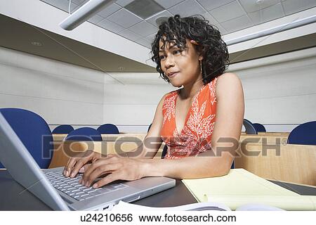Stock Photograph - Female student using laptop in lecture theatre. Fotosearch