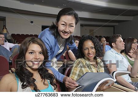 Stock Image - Female teacher assisting female students in class, portrait. Fotosearch