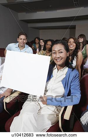 Stock Image - Female teacher holding blank board, in front of class, portrait. Fotosearch