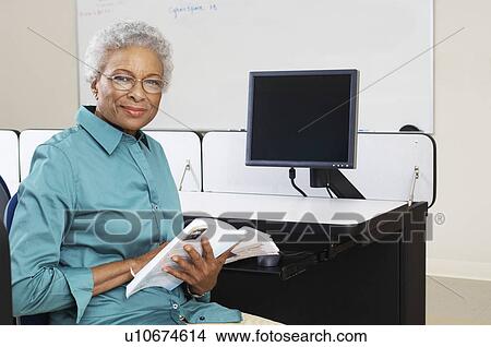 Picture - Female teacher holding book in computer classroom, portrait. Fotosearch
