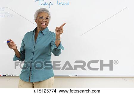 Picture - Female teacher pointing by whiteboard in classroom. Fotosearch
