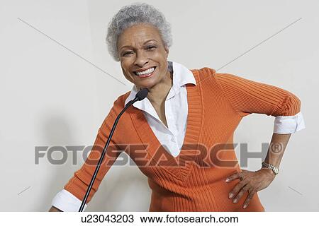 Stock Image - Female teacher using microphone indoors. Fotosearch