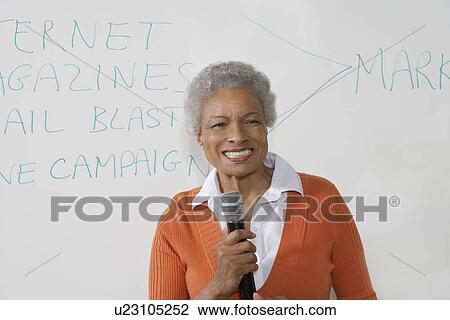 Stock Image - Female teacher using microphone near white board. Fotosearch