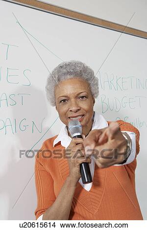 Female teacher using microphone, pointing near white board View Large Photo Image Picture - Female teacher using microphone, pointing near white board. Fotosearch