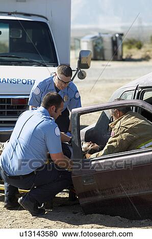 Stock Image - Firefighter and paramedics rescuing victim from crashed car. Fotosearch