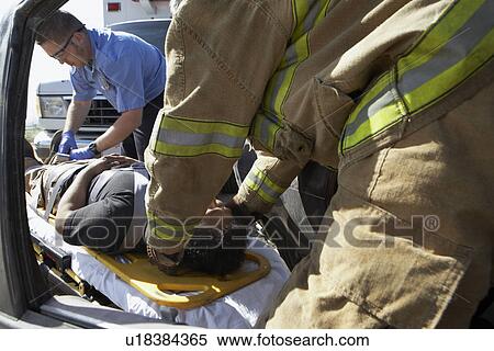 Stock Photography - Firefighter and paramedics taking victim out of crashed car. Fotosearch