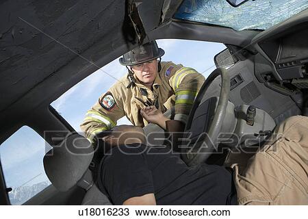 Stock Image - Firefighter looking into crashed car, view from interior. Fotosearch