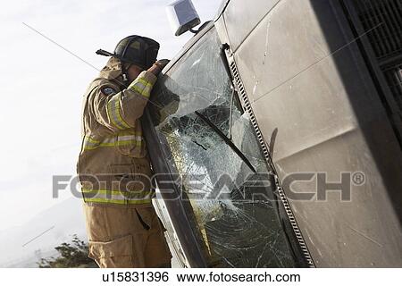 Stock Photograph - Firefighter looking into crashed car. Fotosearch