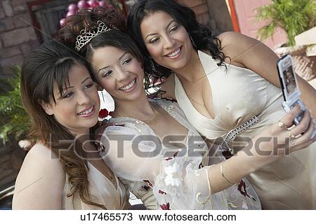 Stock Image - Girl (13-15) taking self-portrait with two friends using mobile phone at Quinceanera. Fotosearch