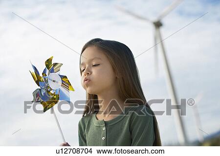 Picture - Girl (5-6) blowing toy windmill at wind farm. Fotosearch
