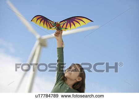 Stock Photo - Girl (5-6) playing with kite at wind farm. Fotosearch